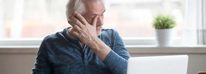 Älterer Mann sitzt vor einem Laptop und hat trockene Augen