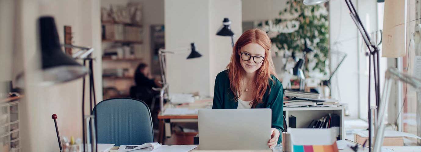 Eine Frau arbeitet an ihrem Laptop und sitzt an einem Schreibtisch