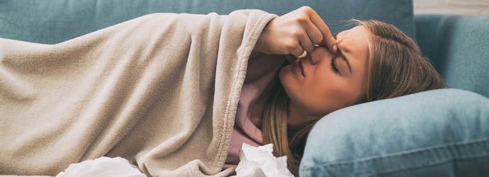Eine Frau mit Nasennebenhöhlenentzündung liegt auf einem blauen Sofa