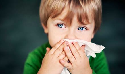 Ein Junge mit Hausstauballergie hält sich ein Taschentuch vor die Nase