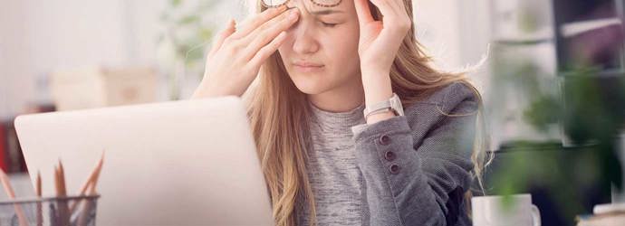Eine junge Frau leidet unter tränenden Augen während sie an einem Laptop arbeitet