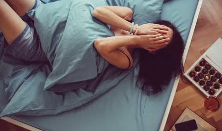 Een vrouw ligt op bed met een kussen op haar buik en haar handen voor haar gezicht