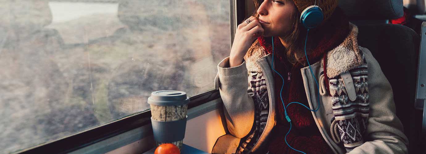 Een vrouw gekleed in winterkleding met print kijkt uit een raam van de trein terwijl ze een koptelefoon draagt