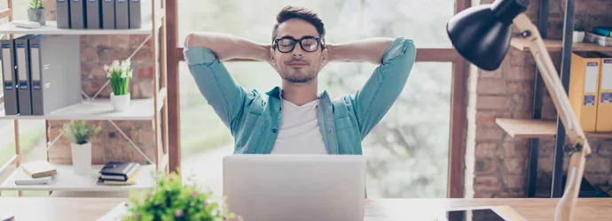 Een zeer ontspannen man leunt achterover in een stoel achter een bureau in een modern kantoor met zijn handen achter zijn hoofd