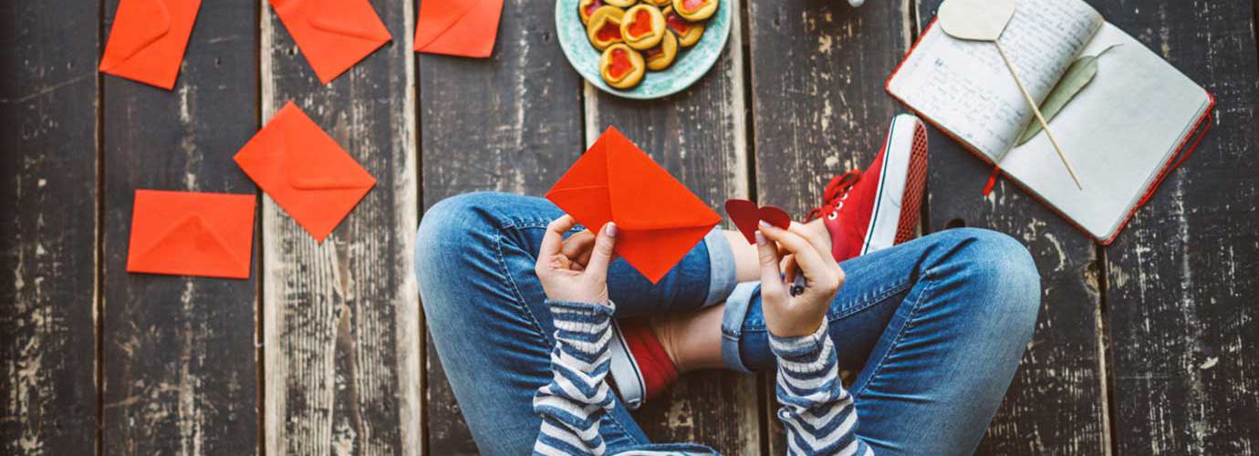 Een vrouw schrijft valentijnskaarten met zelfgemaakte valentijnscadeautjes terwijl ze op de vloer zit