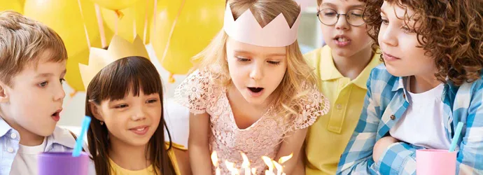 Gruppe junger Kinder an einem Tisch mit Luftballons, Kuchen auf einer Geburtstagsparty für Kinder