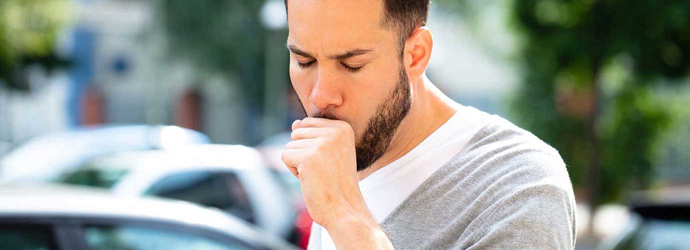 Man hoest buiten omringd door auto's