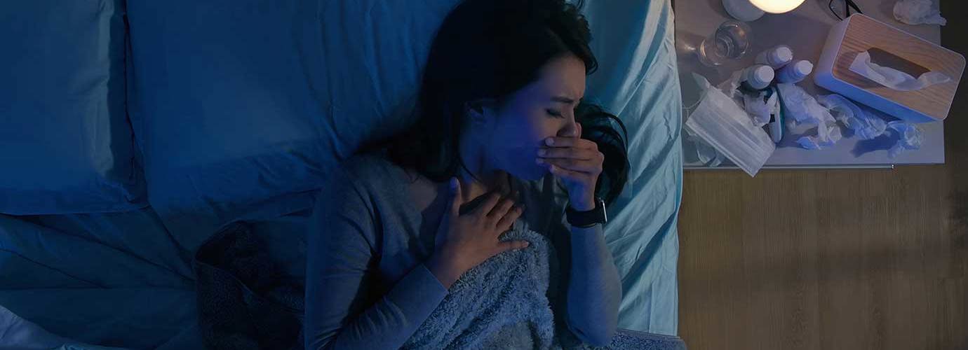 Vrouw in bed hoest 's nachts naast een nachtkastje met medicijnen