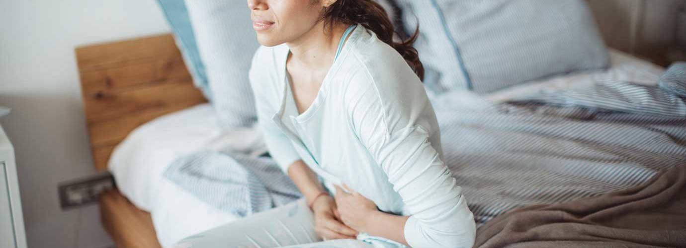 Donna seduta sul suo letto con dolori addominali
