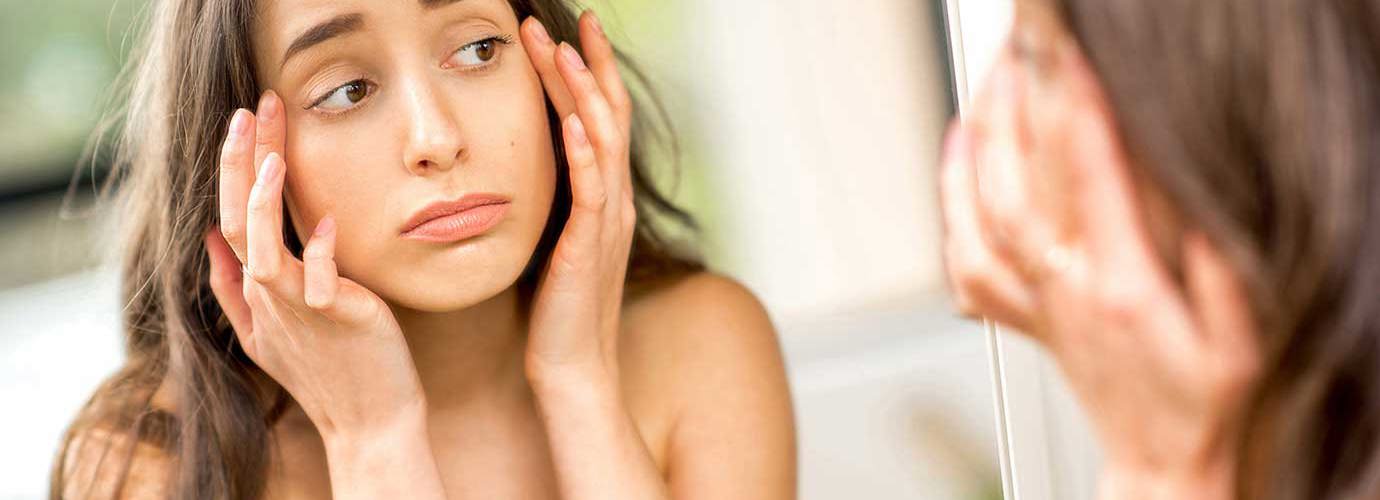 Adolescente controlla allo specchio gli occhi gonfi provocati dalle allergie 